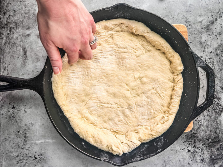 A hand working the dough into the cast iron skillet.