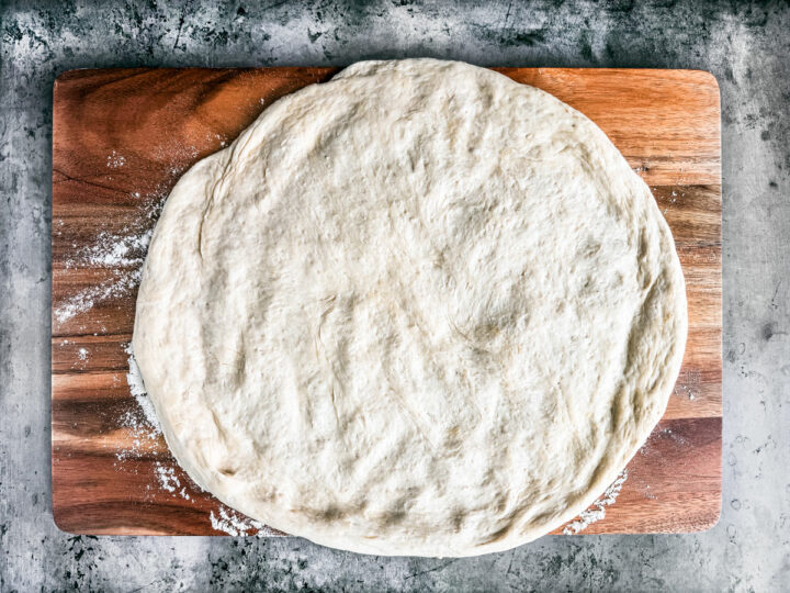Fresh pizza dough worked out into a circle on a floured cutting board.