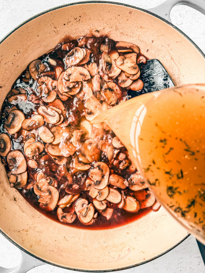 Chicken broth being poured into the pan with the red wine and mushrooms.