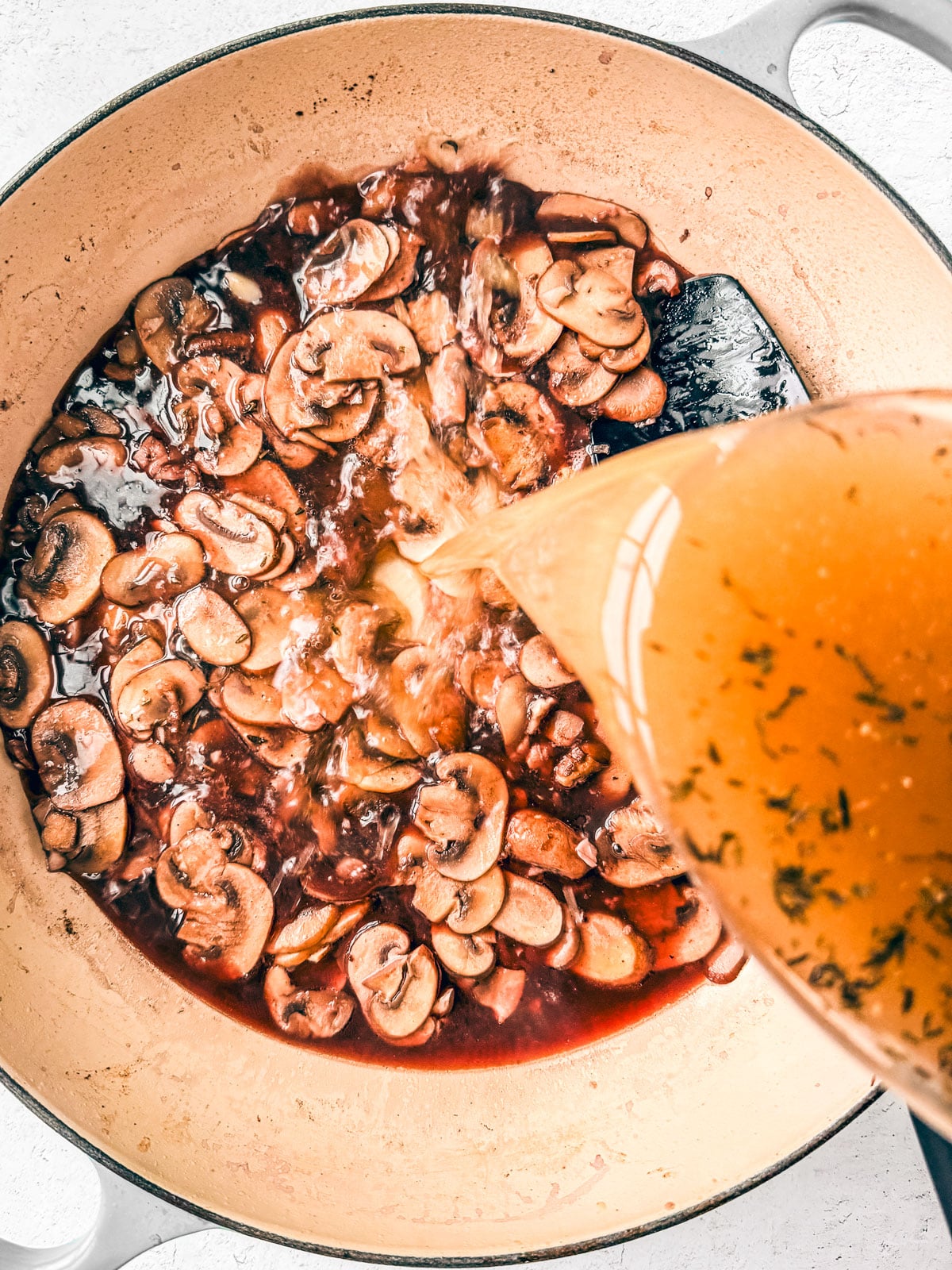 Chicken broth being poured into the pan with the red wine and mushrooms.