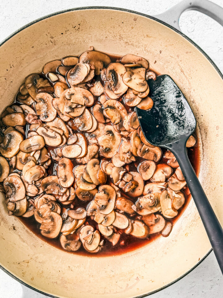 Red wine added to the cooked mushrooms in a pan.