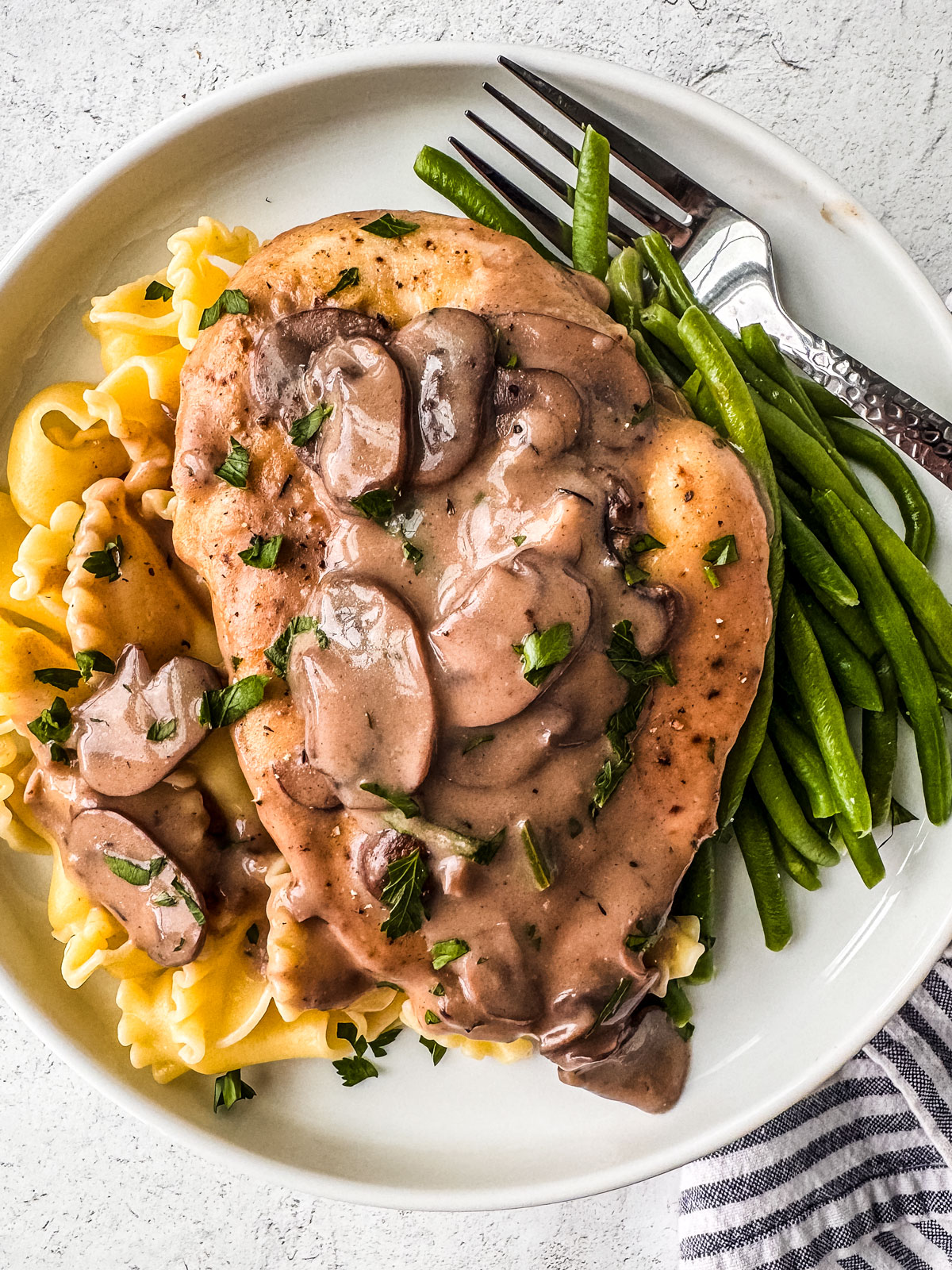 A chicken cutlet smothered in creamy mushroom sauce served over noodles and green beans.