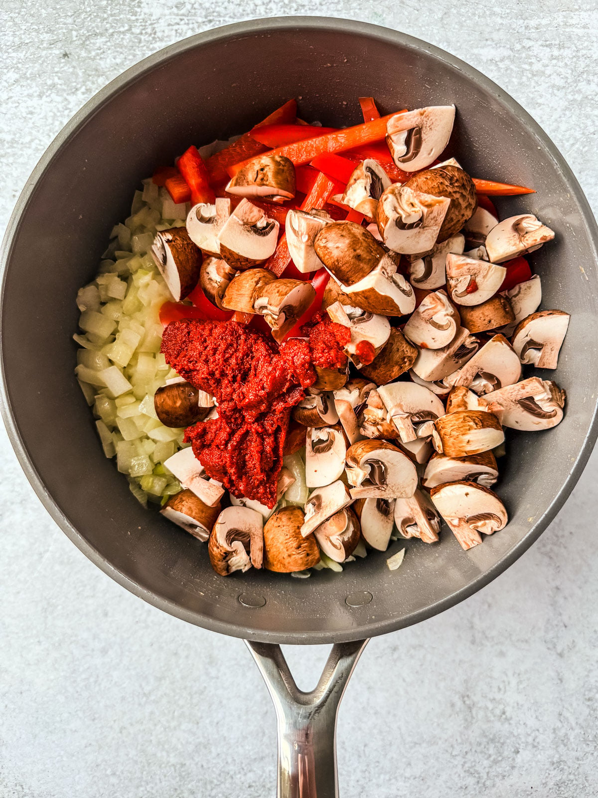 Pan holding cooked onions with mushrooms, peppers, and red curry paste added.