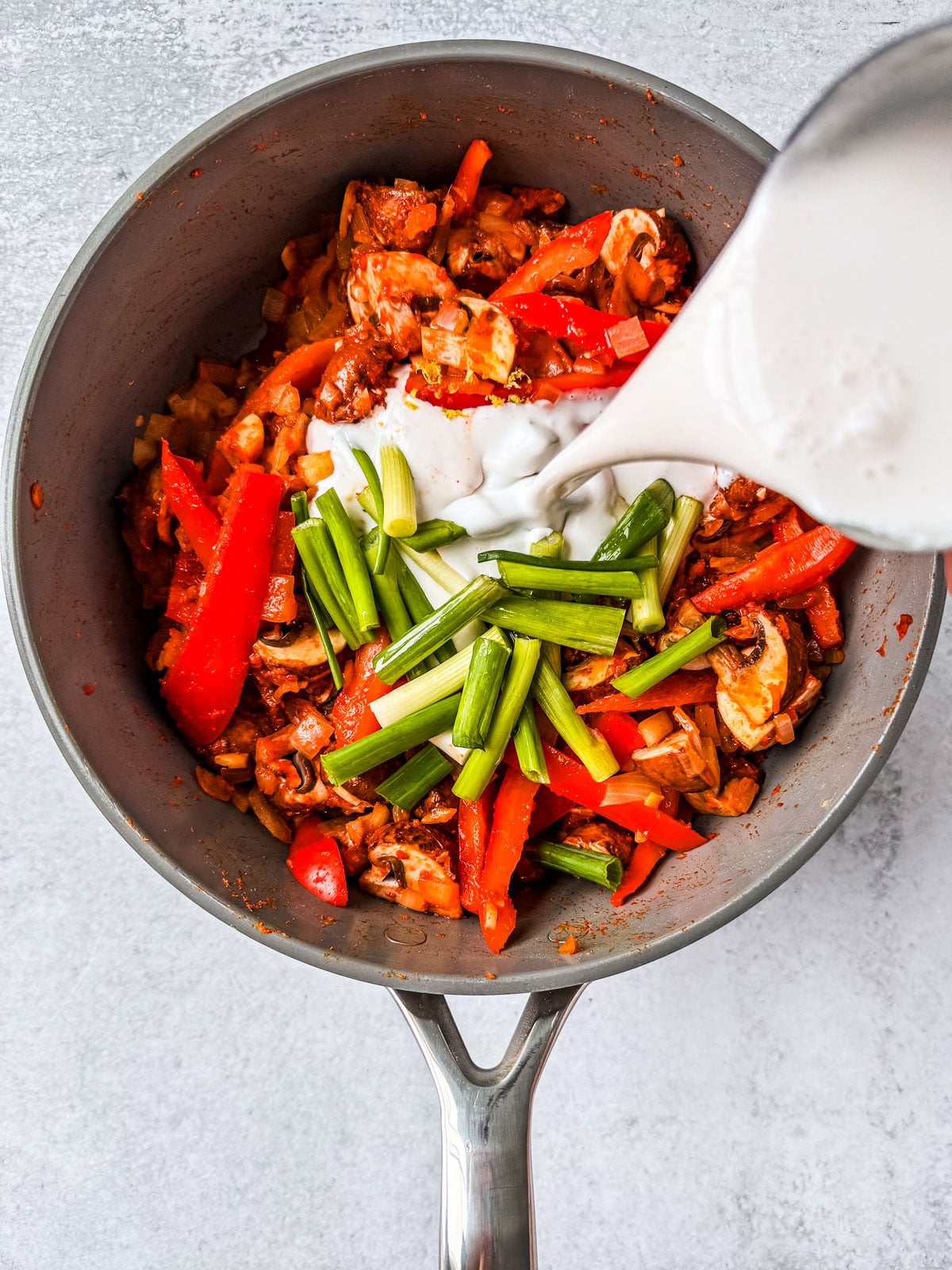 Coconut milk being added into the pan of veggies.