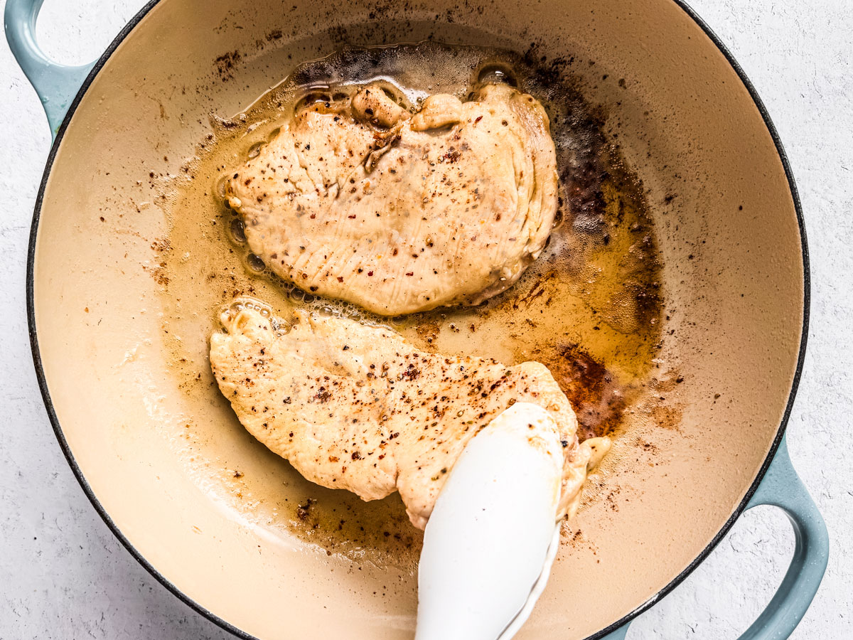 Chicken cutlets being cooked in a pan with oil.