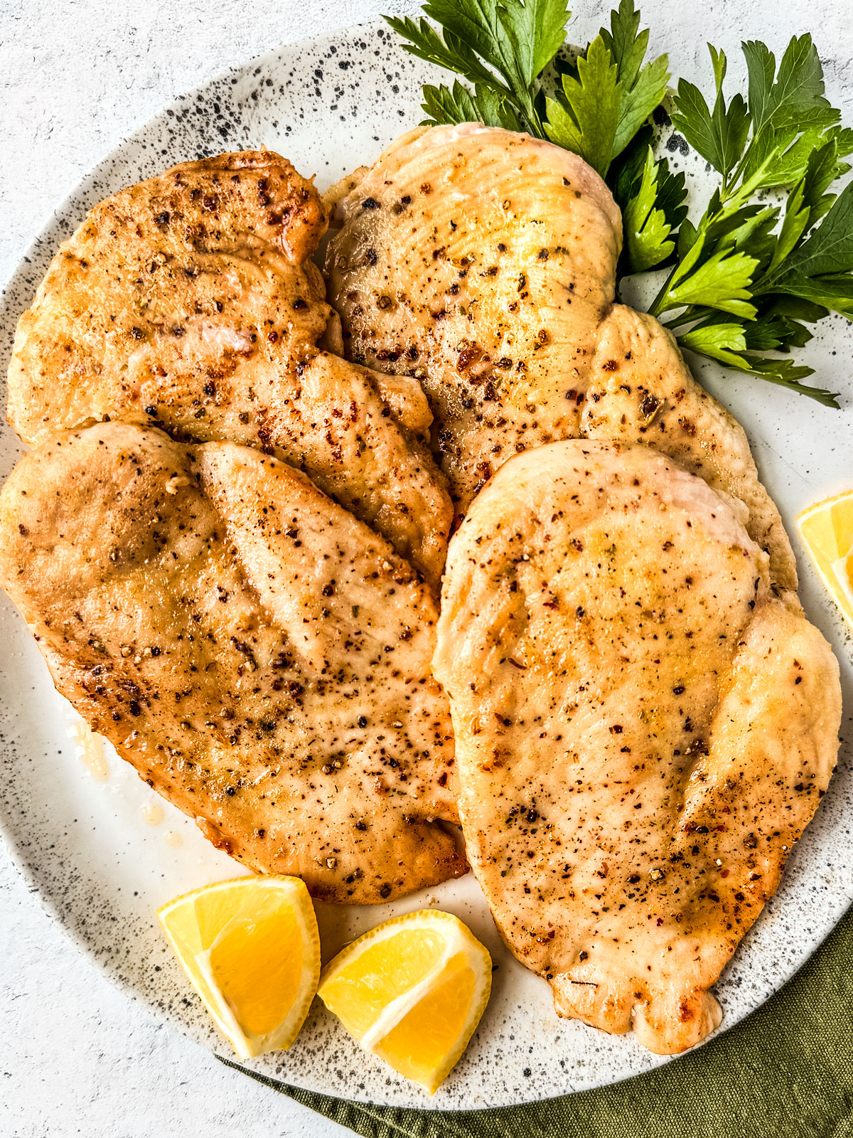 Seasoned chicken cutlets on a plate with lemon wedges and fresh parsley.