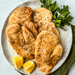 Plate of cooked chicken cutlets with lemon wedges and parsley.