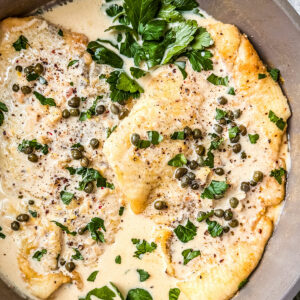 Flounder fillets in a pan smothered in creamy lemon caper sauce.