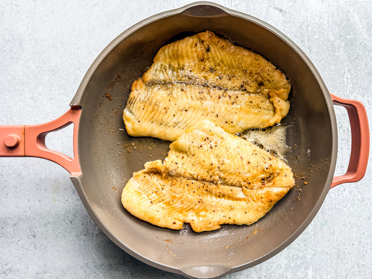 Flounder fillets fried golden in a skillet.