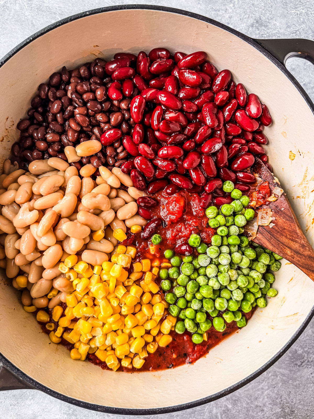 Beans, corn, peas, and tomatoes dumped into pot in colorful segments.
