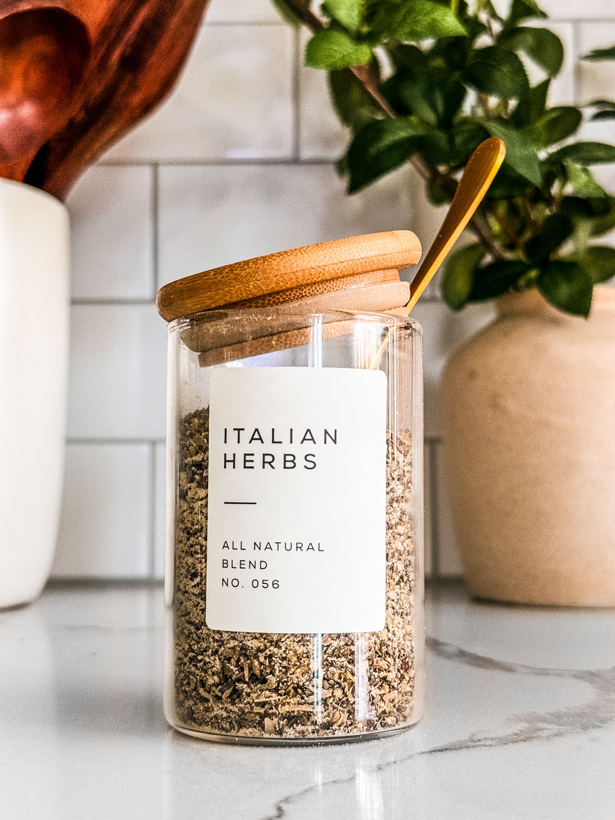 Glass jar of Italian seasoning on a white marble kitchen countertop.