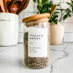 Glass jar of Italian seasoning blend on a marble countertop.