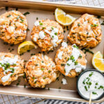 Tray of jumbo lump crab cakes with lemon wedges and yogurt sauce.