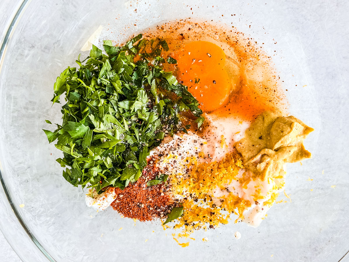 Egg, parsley, spices, yogurt, mayo, and mustard in a mixing bowl. 