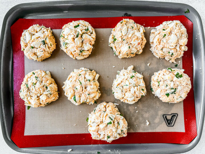 Crab cakes formed and set on a baking sheet, uncooked.
