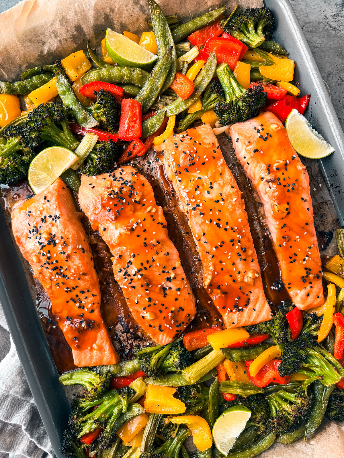 Sheet pan salmon with veggies and lime wedges.