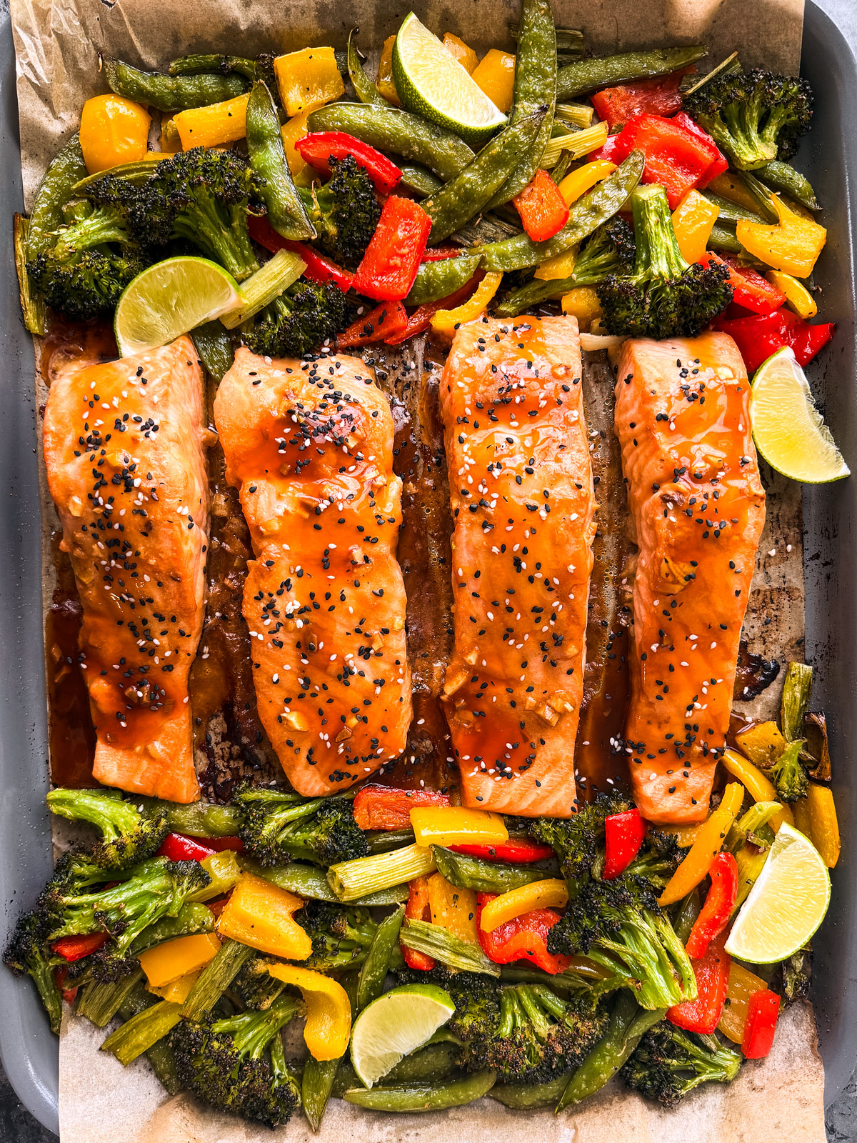 Cooked salmon fillets on a sheet pan with roasted vegetables.