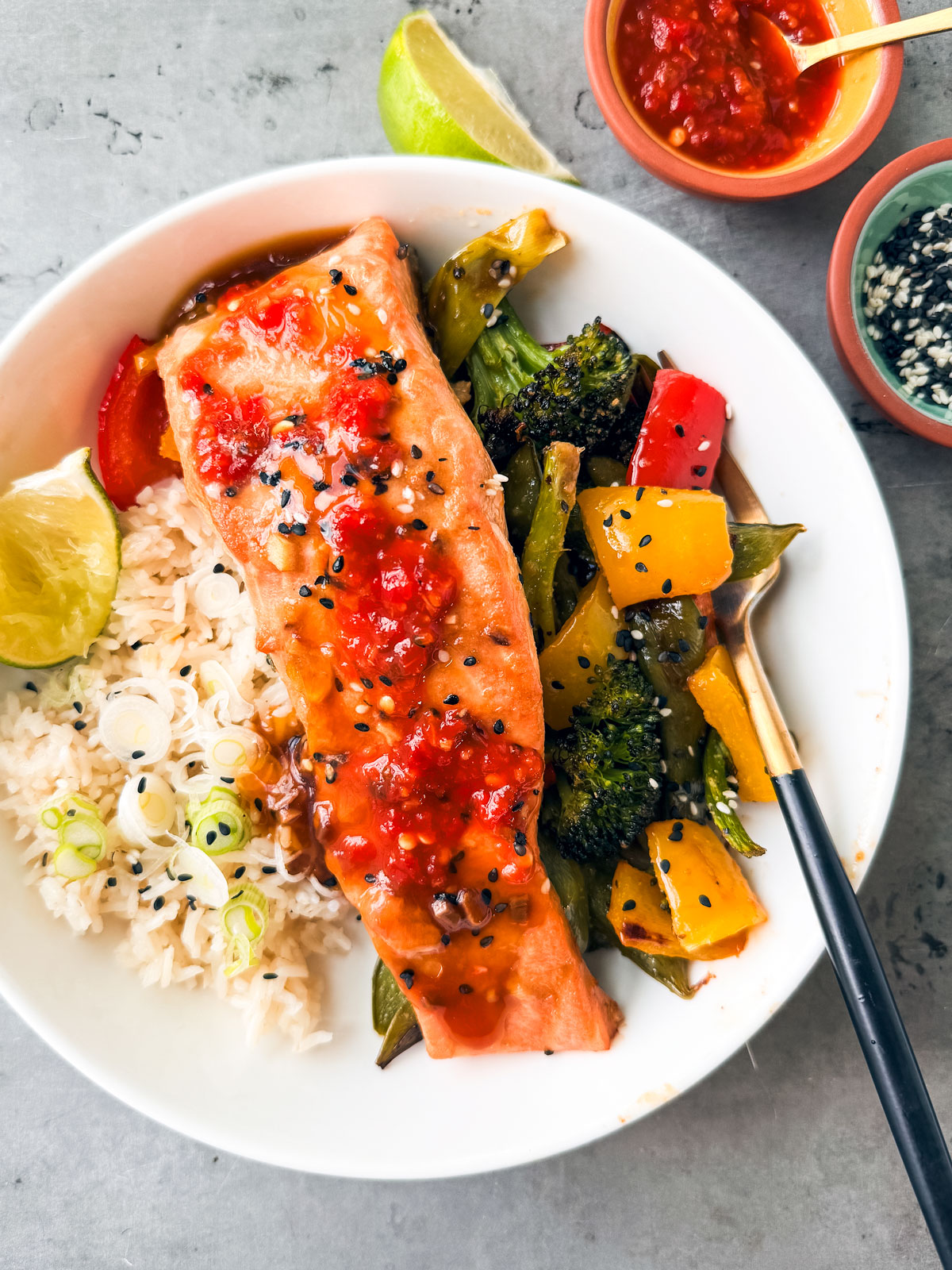 Salmon fillet with chili sauce over vegetables and rice on a plate.