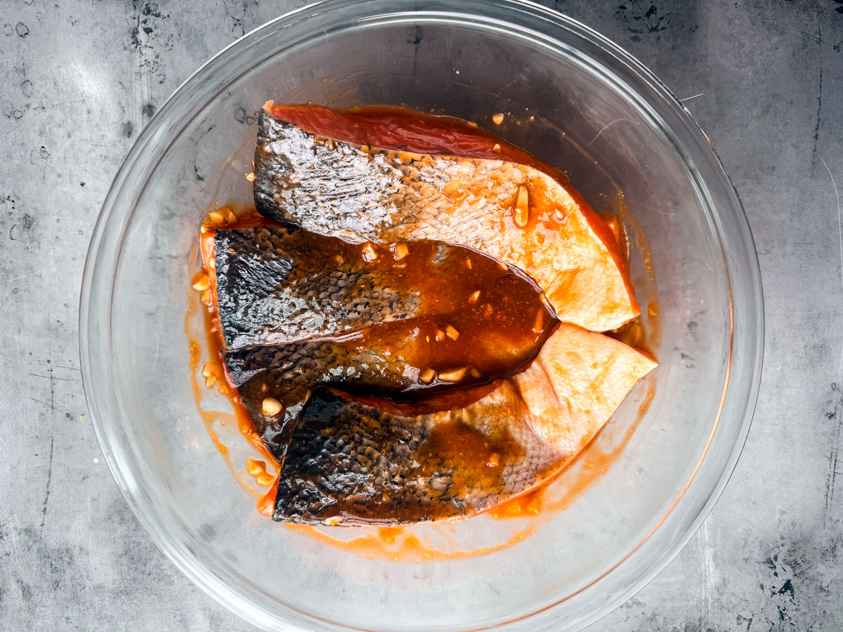 Salmon fillets in a marinade in glass bowl.
