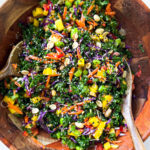 Rainbow salad in a bamboo bowl with bamboo serving spoons.