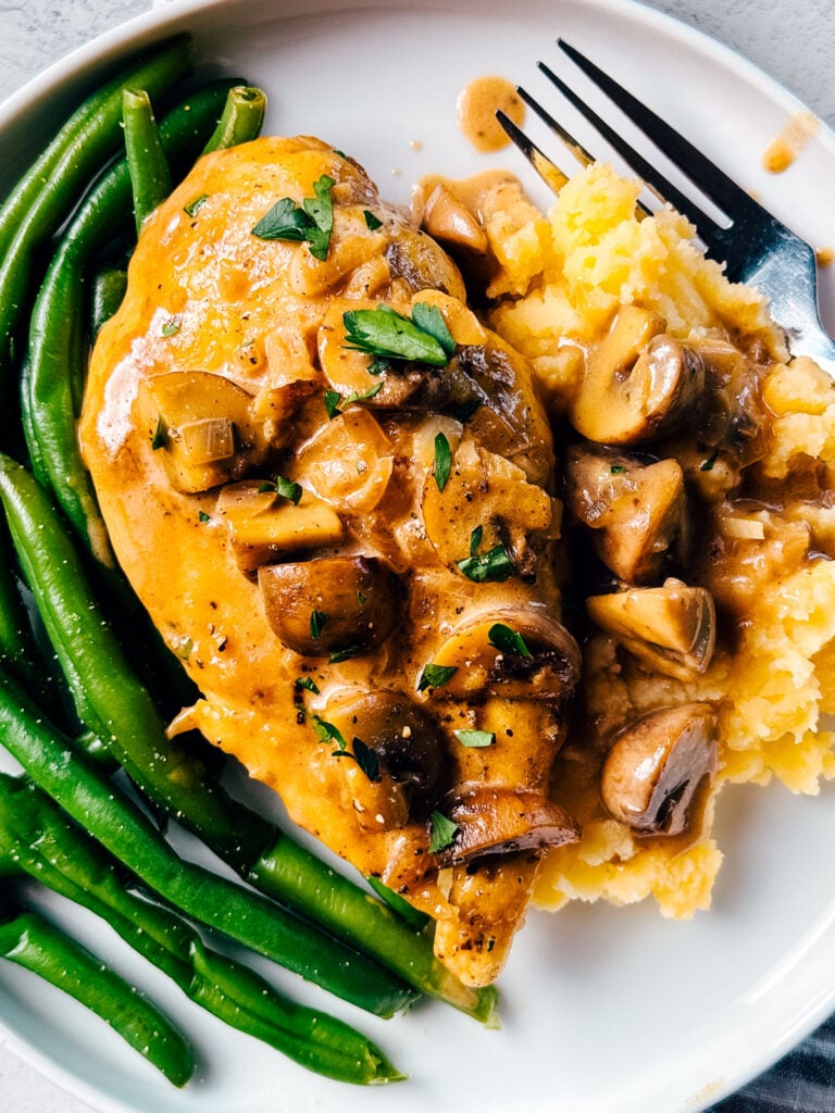 A plate of chicken Marsala with green beans and mashed potatoes.