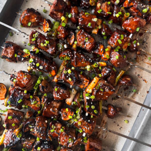 Beef skewers piled up on a baking sheet.