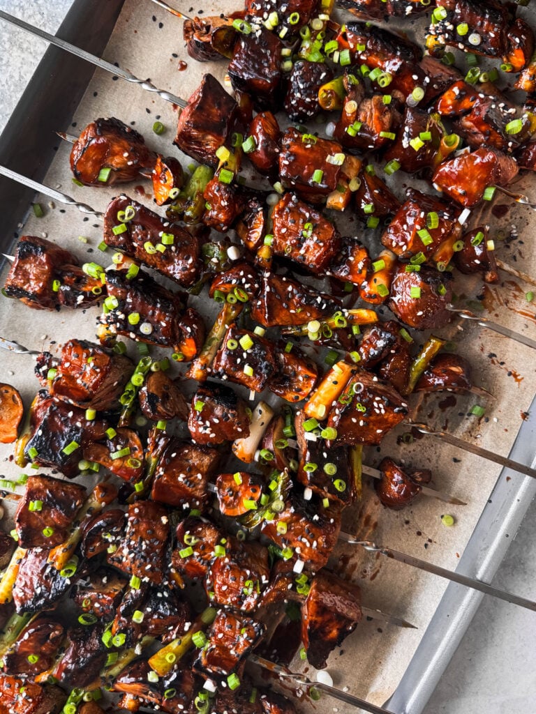 Beef skewers piled up on a baking sheet.
