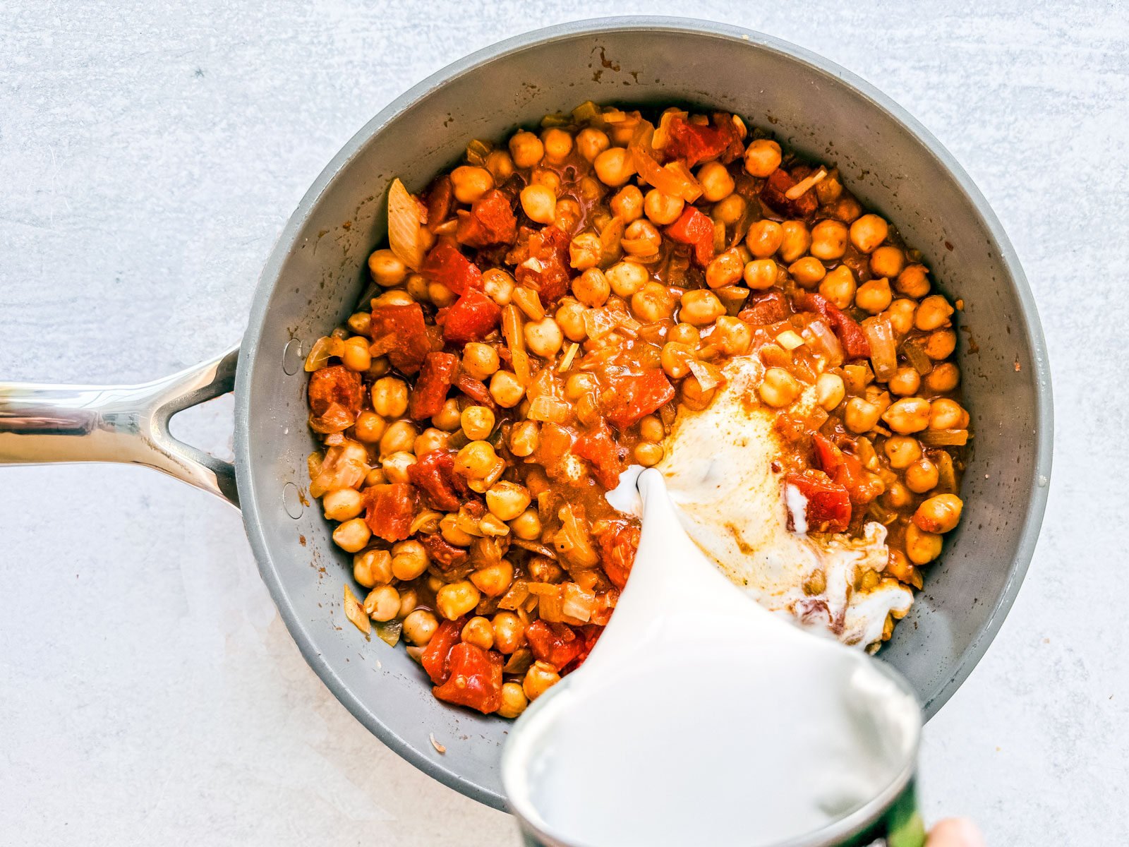 Coconut milk being added to a pan with spiced chickpeas and tomatoes.