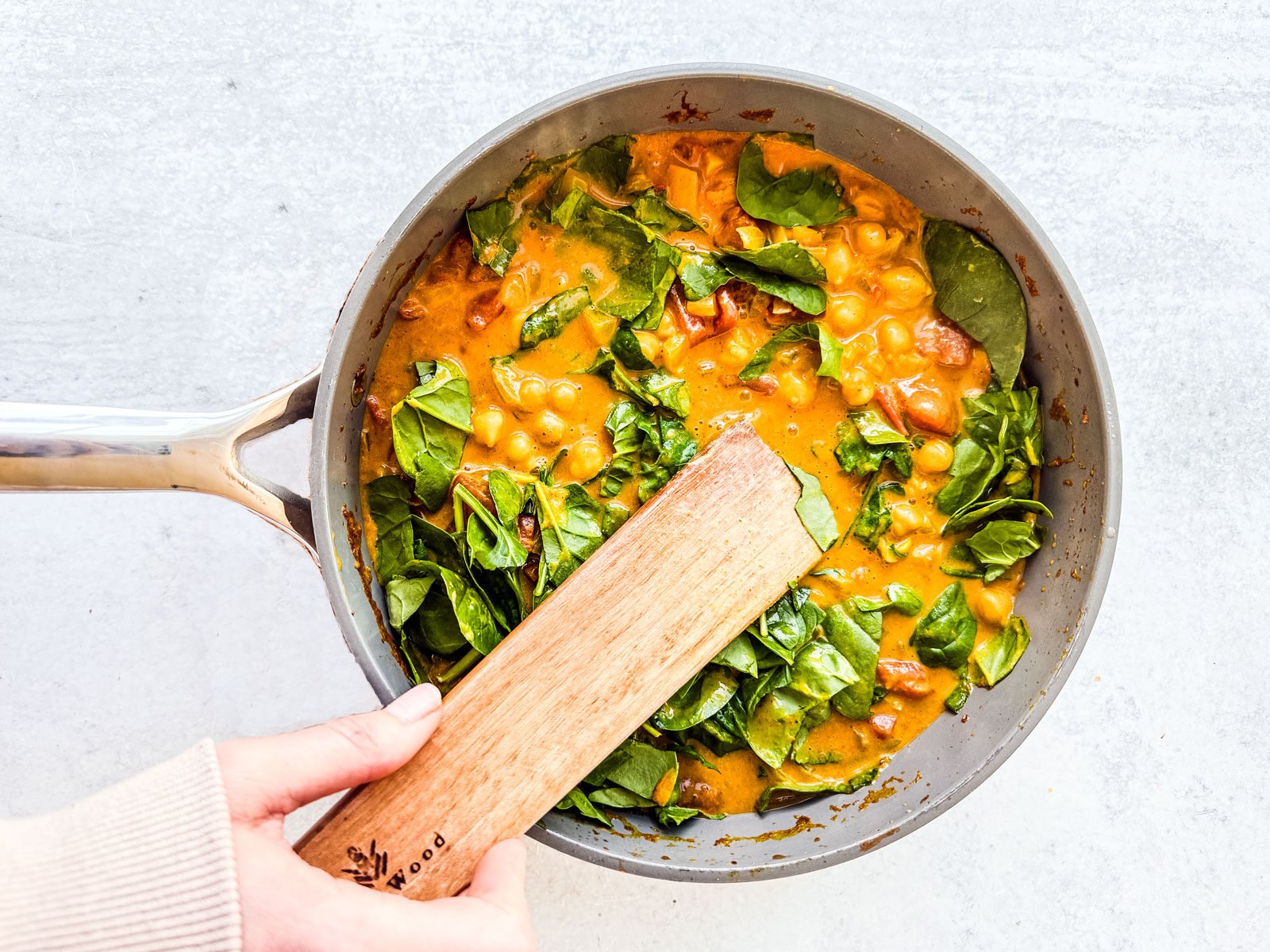 Baby spinach being stirred into pan of chickpea curry.