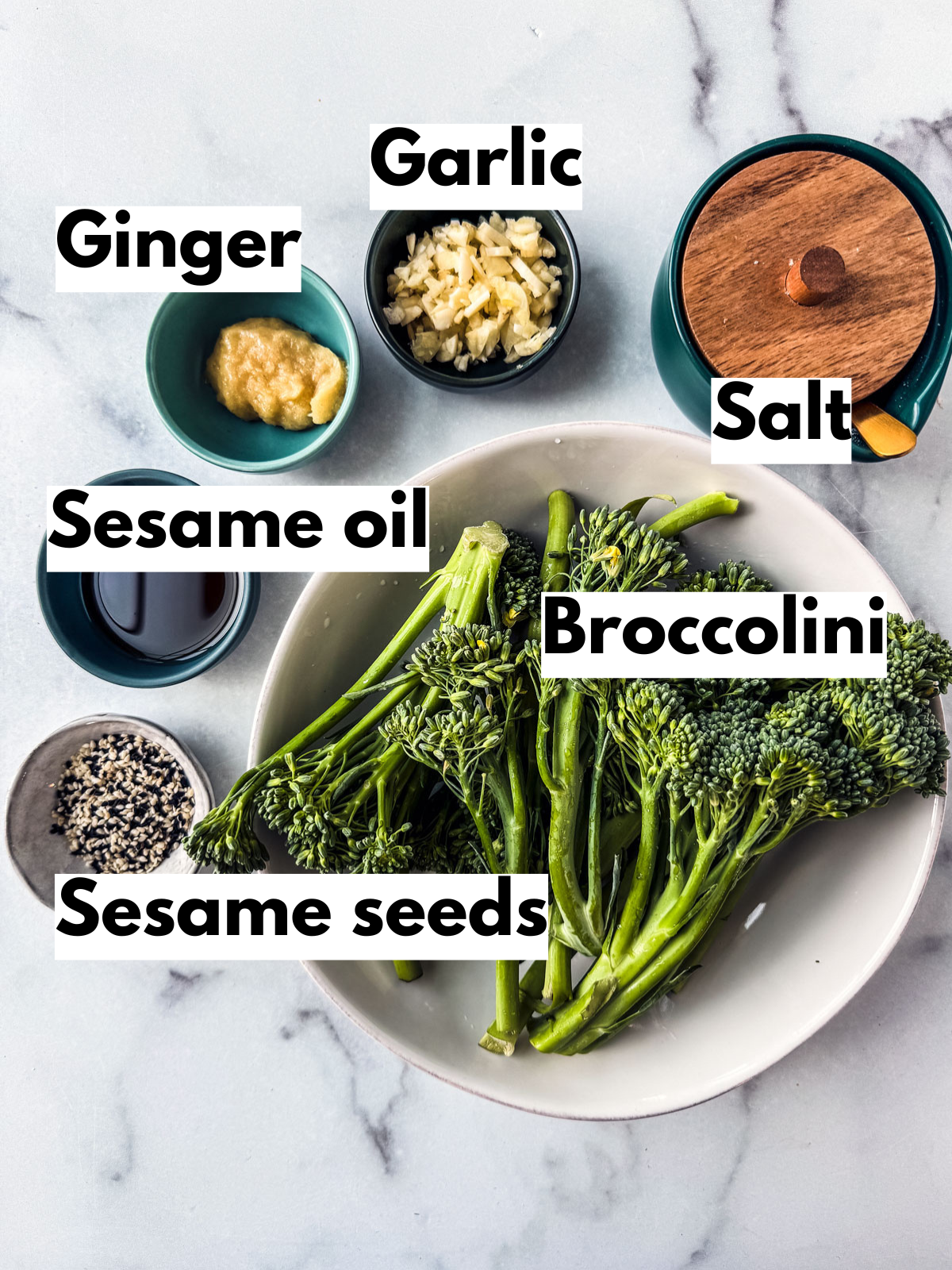 Ingredients for garlic ginger saut&eacute;ed broccolini spread out over a white marble background. 