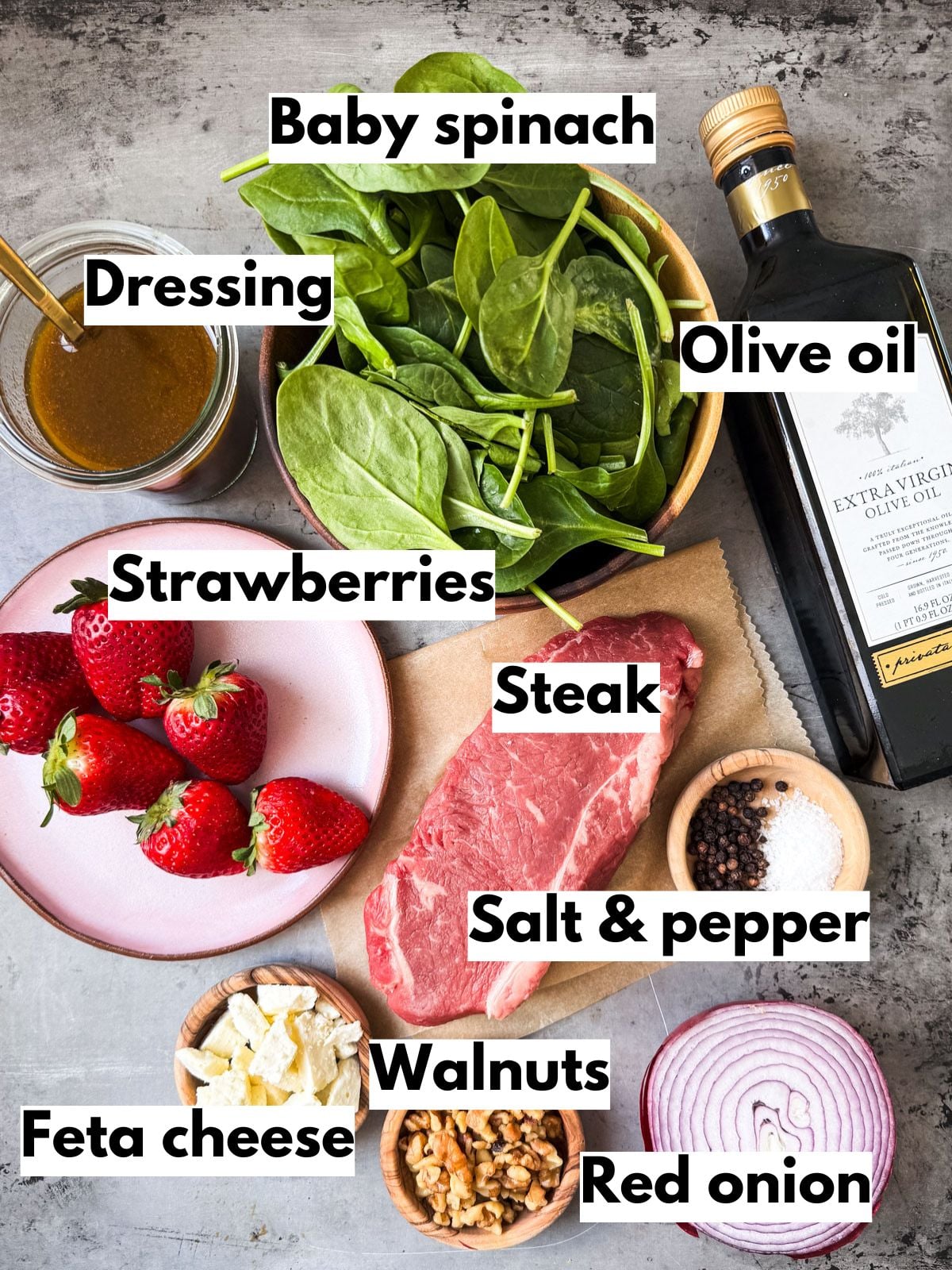 Ingredients to make Strawberry Spinach Salad and steak on a dark stone background.