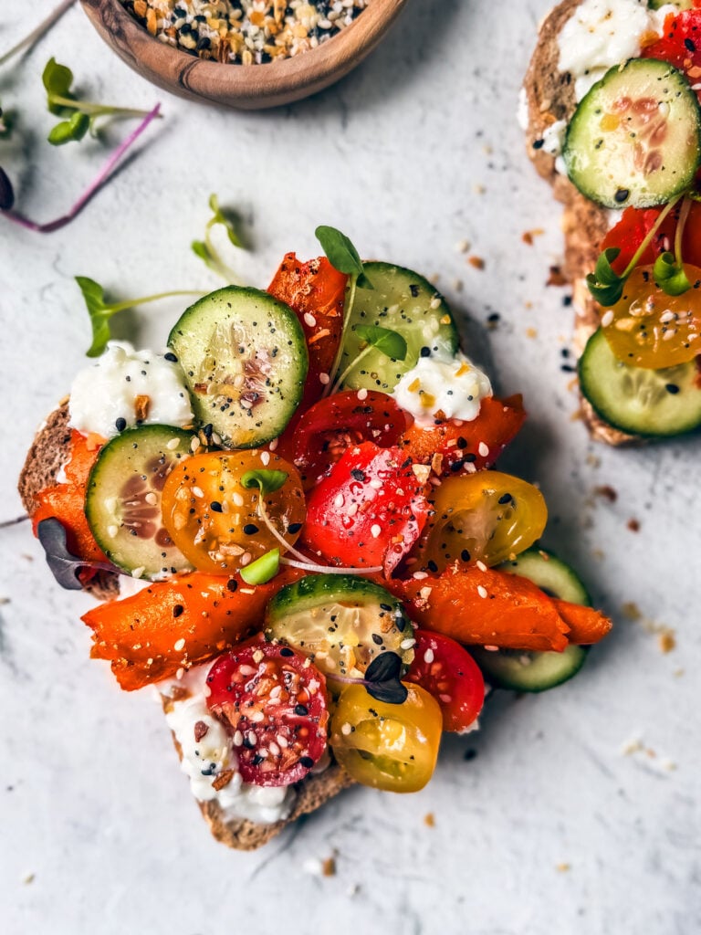 Cottage cheese toast topped with smoked salmon, tomatoes, cucumbers, and seasoning.