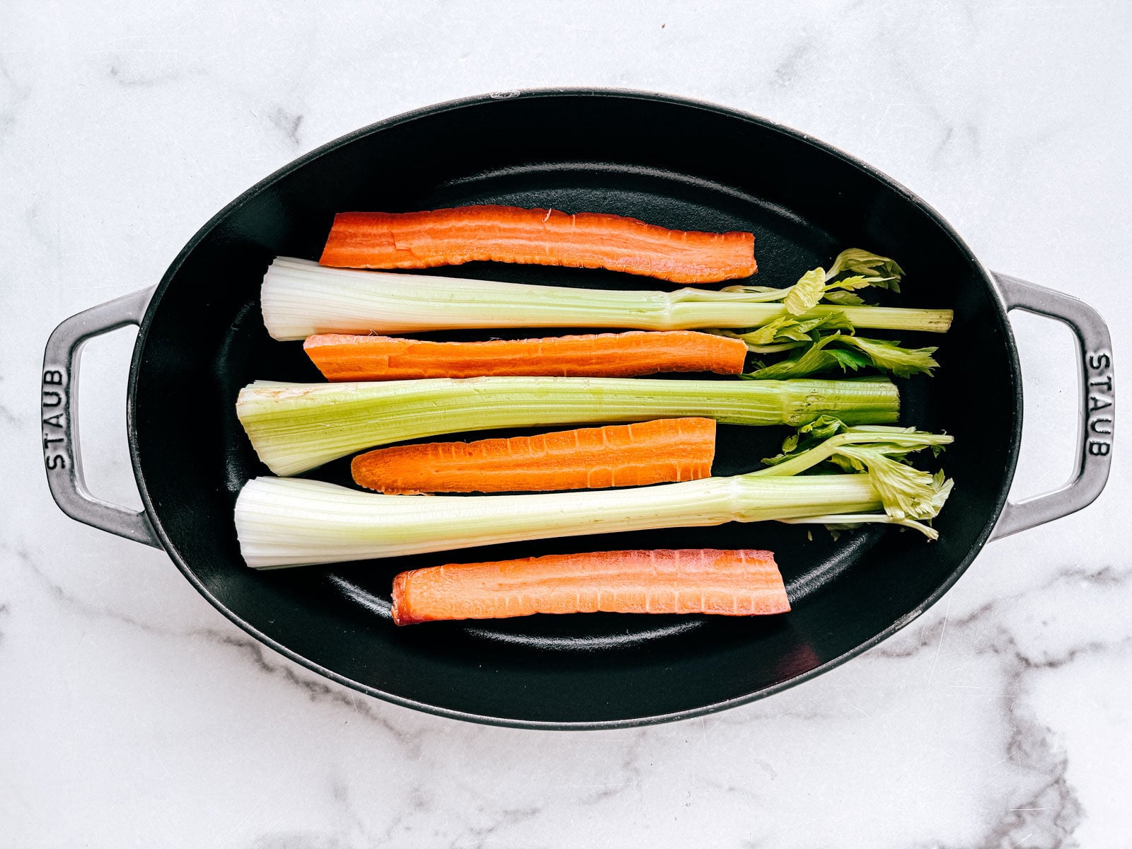Celery stalks and carrots in a roasting pan.