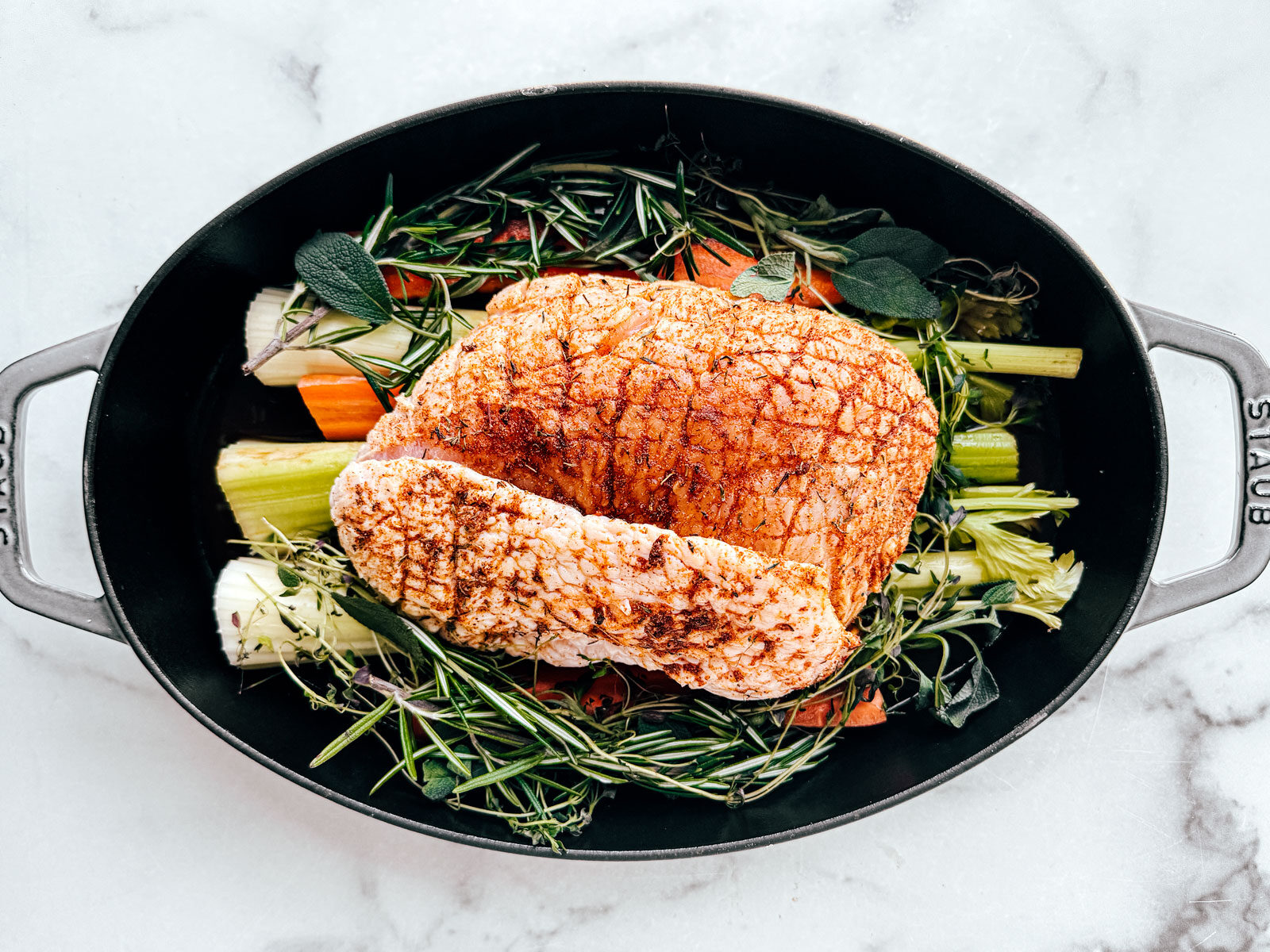 Turkey breast in a roasting pan with veggies and herbs.