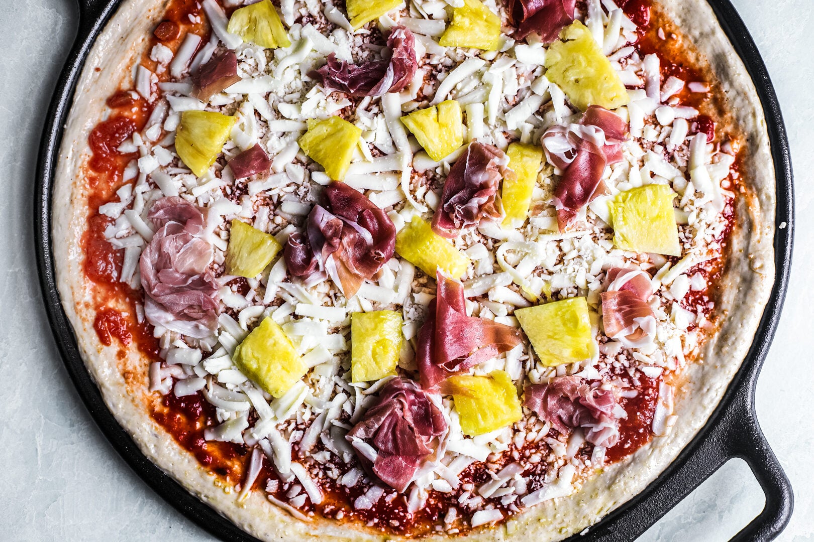 Hawaiian pizza on cast iron pan, uncooked.