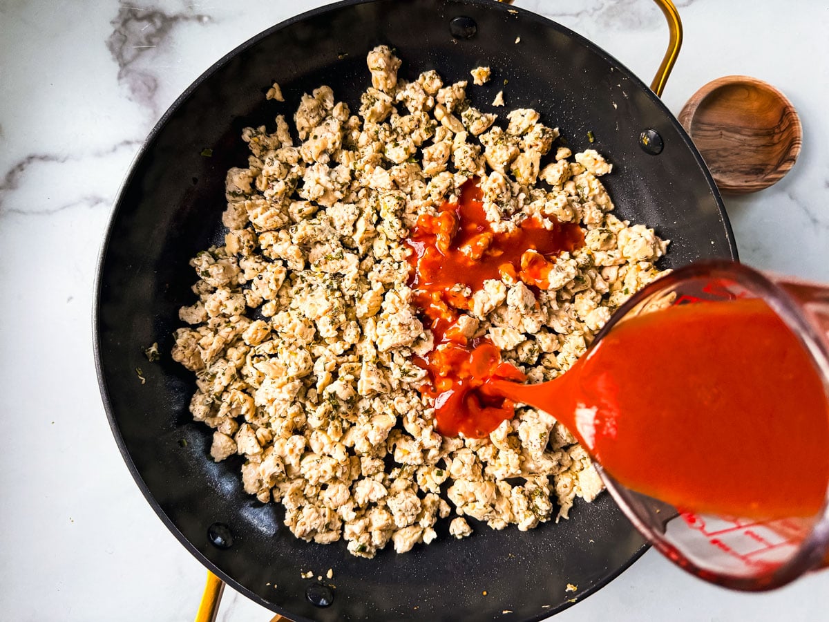 Pan of cooked ground chicken with hot sauce being poured over it.
