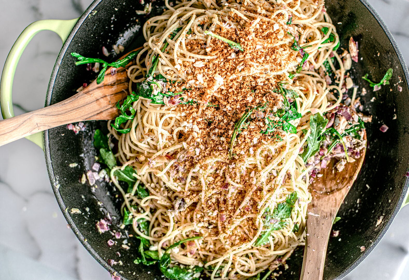 Pasta stired up in a pan with arugula and toasted breadcrumbs.