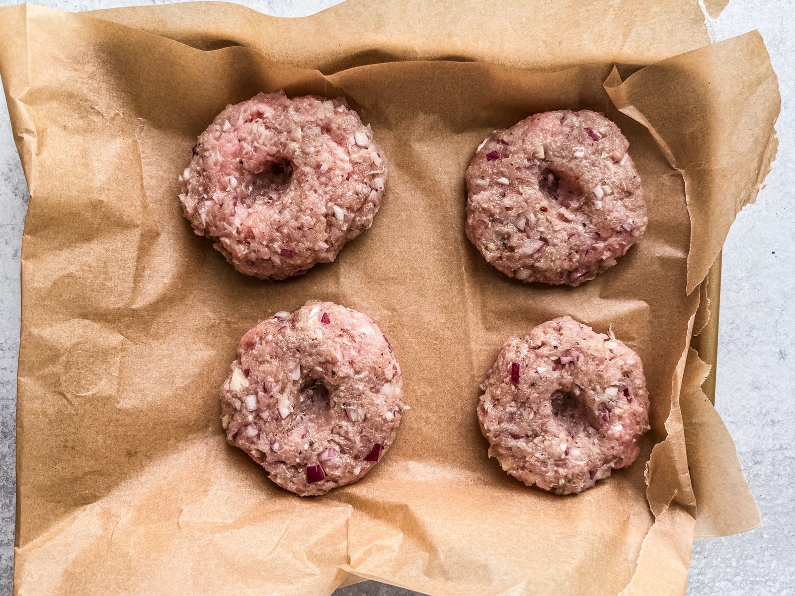 Formed uncooked patties, with a divot in the middle of each, on baking sheet.