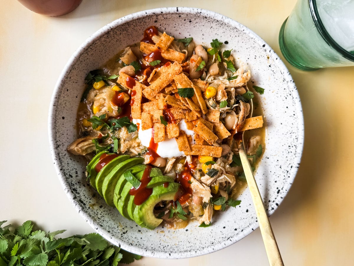 White chicken chili in a bowl topped with sliced avocado and tortilla strips.