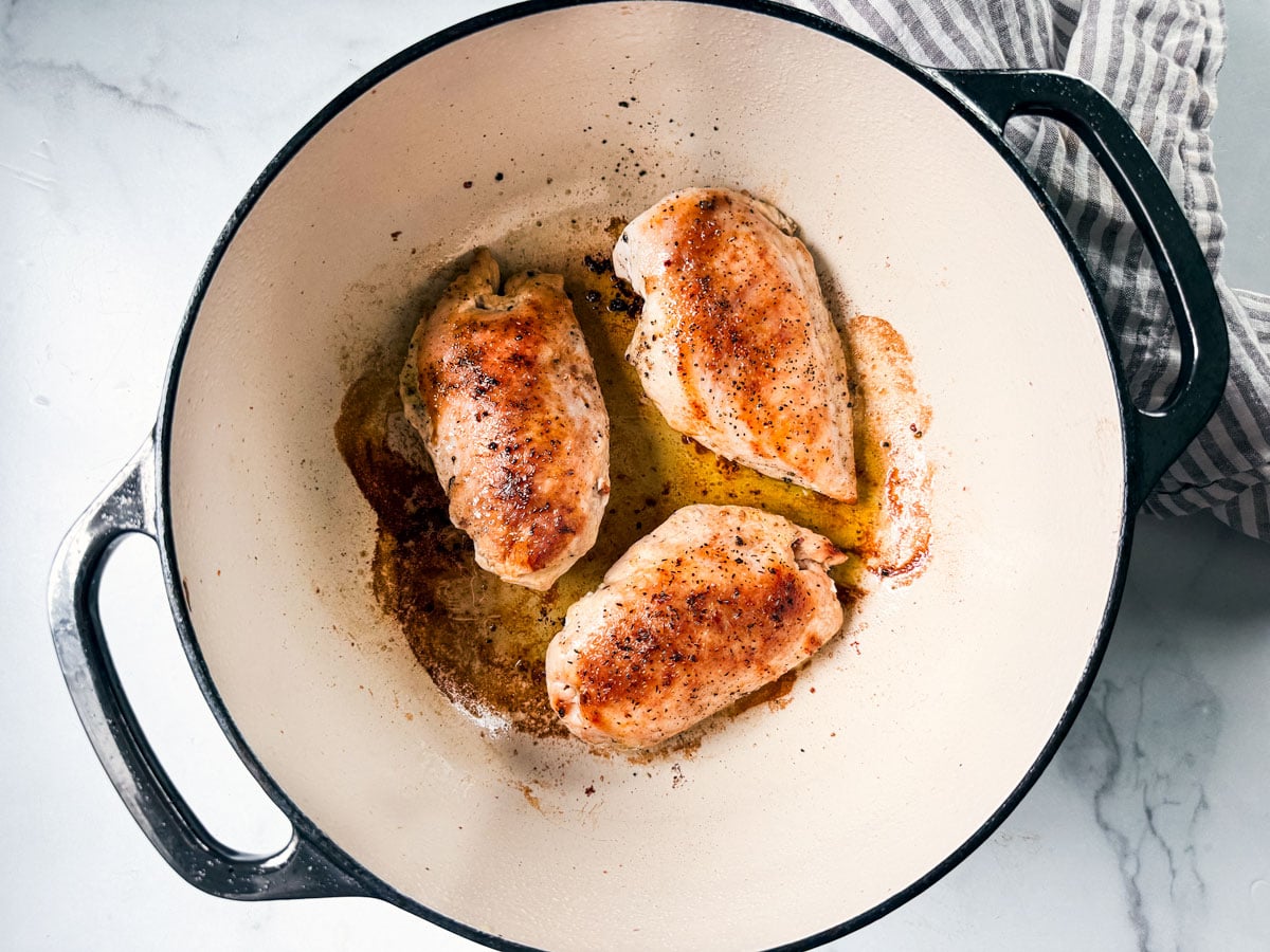 Dutch oven with cooked chicken breasts in it.