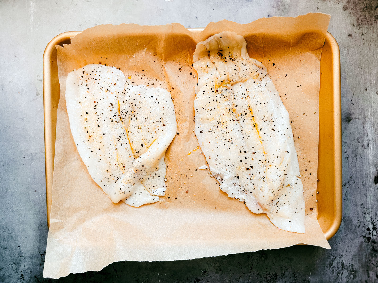 Salt and pepper-seasoned fish fillets on a parchment-lined baking sheet.