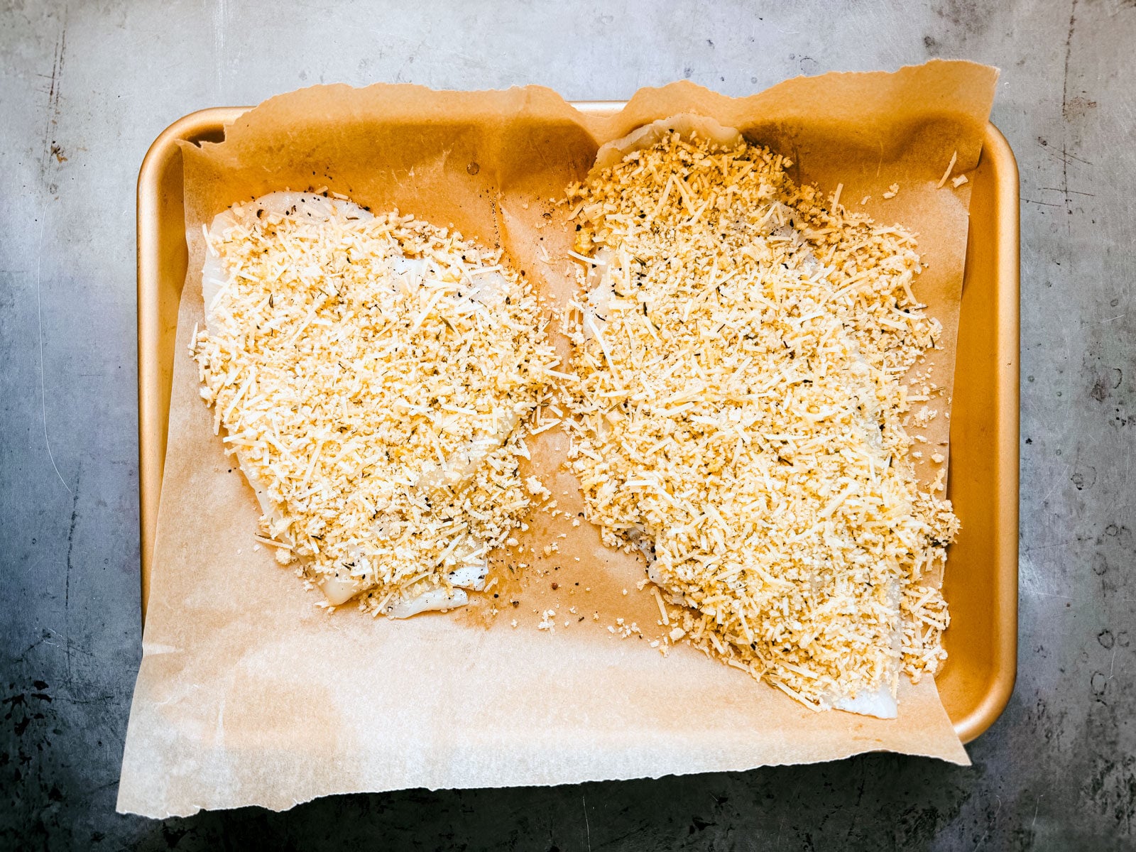 Flounder fillets uncooked, covered in bread crumb and parmesan mixture.