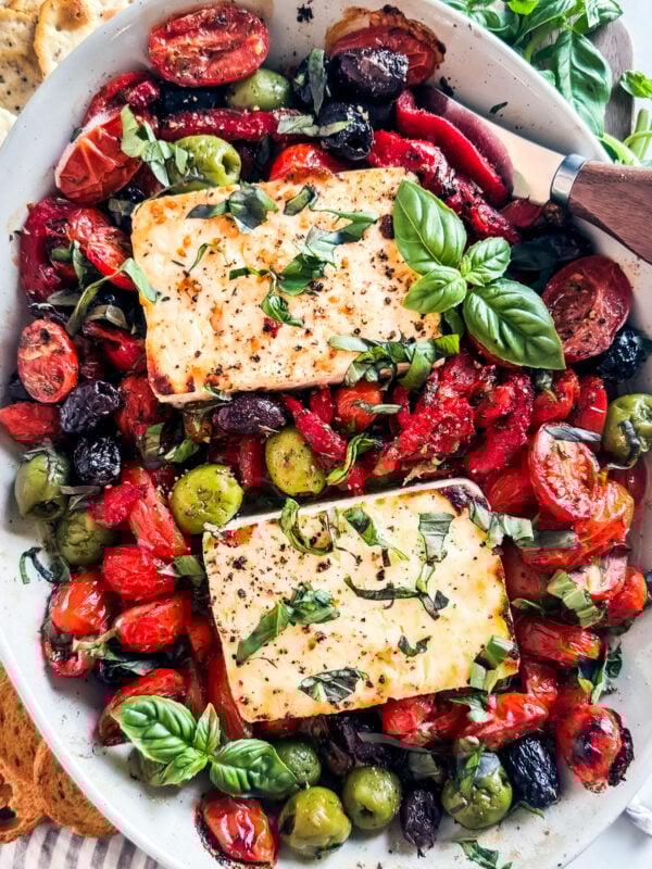 Baked feta in a baking dish with tomatoes, olives, and fresh basil.