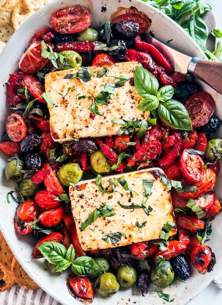 Baked feta in a baking dish with tomatoes, olives, and fresh basil.