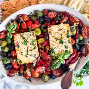Baked feta in a baking dish with tomatoes, olives, and fresh basil.