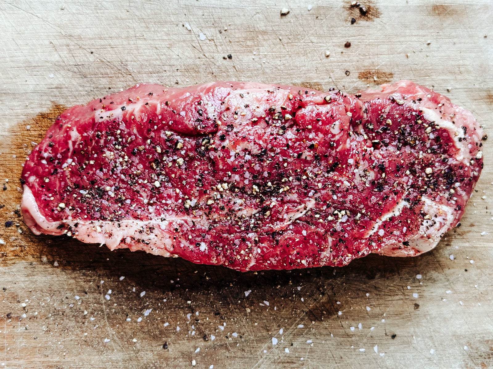 Raw steak on a cutting board seasoned with salt and pepper.