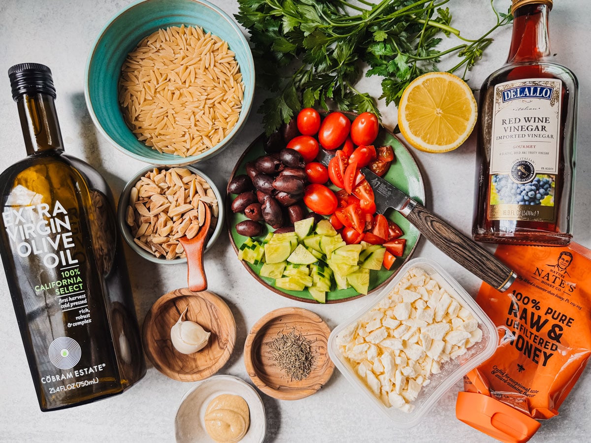 Ingredients for Mediterranean orzo pasta salad on a white background.