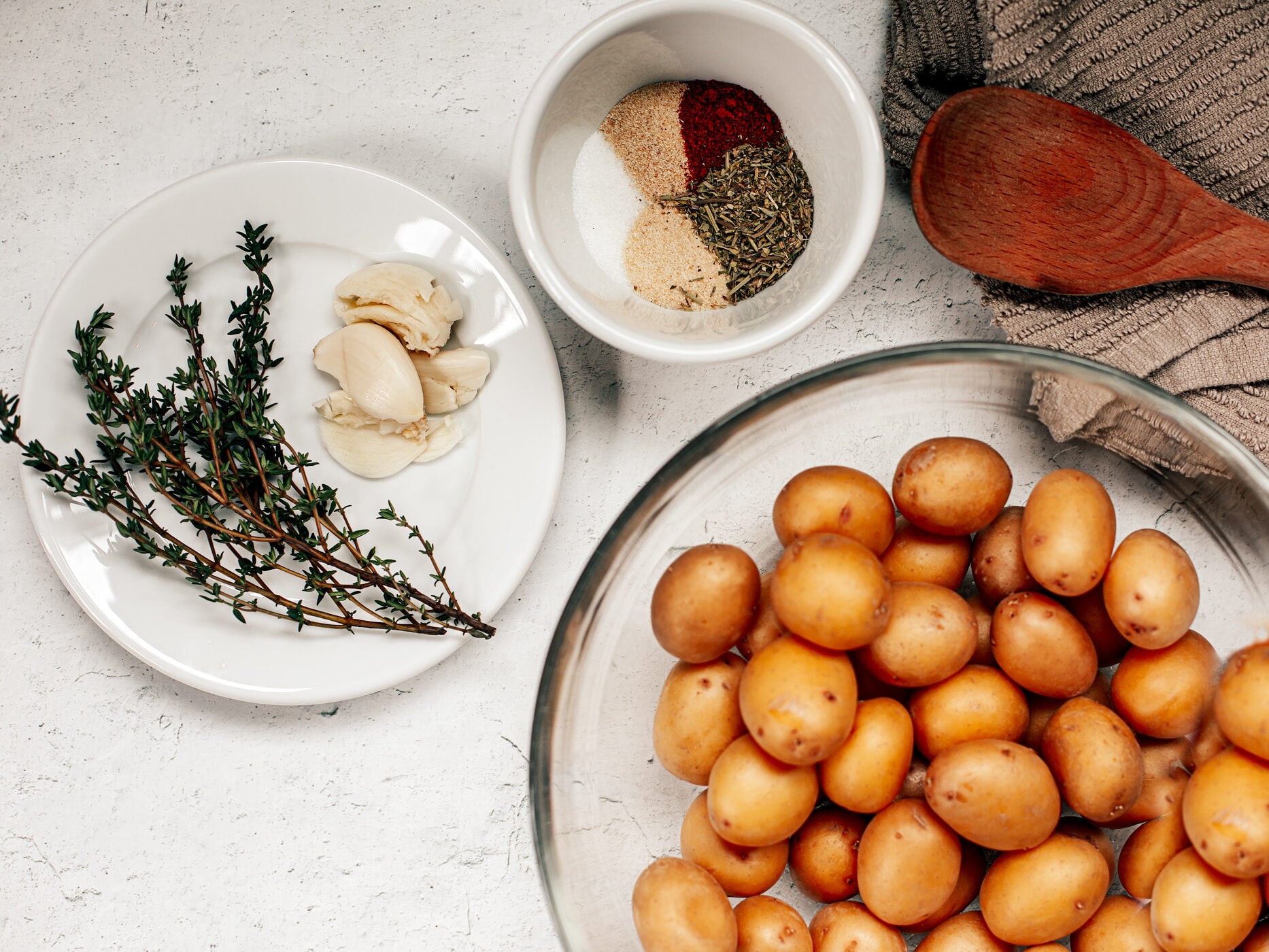 Mini potatoes in a glass bowl with fresh thyme, garlic, and seasoning.