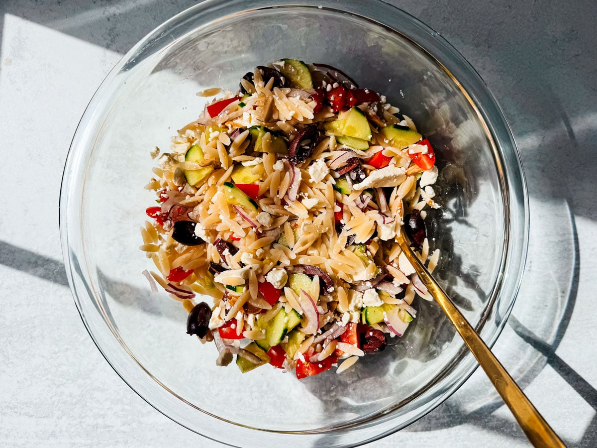 Orzo pasta salad in a mixing bowl with veggies and feta.