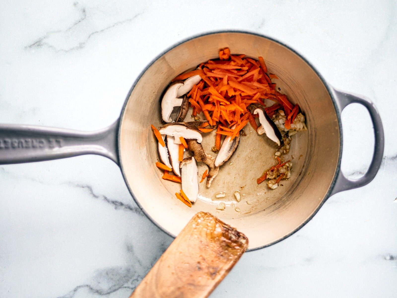 Mushrooms and shredded carrots in a saucepan with garlic and ginger.